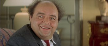 Movie still from “Le Dîner de Cons” (1998), directed by Francis Veber – A person wearing a suit and tie smiling; Close Up shot, Low angle