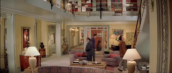 Movie still from “Le Dîner de Cons” (1998), directed by Francis Veber – Two people standing in a living room next to each other; Wide shot, High angle