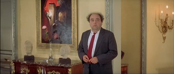 Movie still from “Le Dîner de Cons” (1998), directed by Francis Veber – A man in a suit standing in front of a painting; Medium shot, Low angle