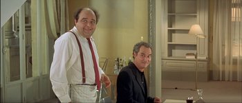 Movie still from “Le Dîner de Cons” (1998), directed by Francis Veber – Two men standing next to each other in front of a wall; Medium shot, Low angle