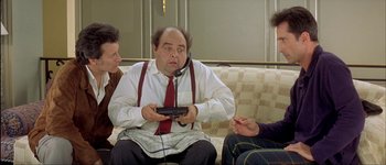 Movie still from “Le Dîner de Cons” (1998), directed by Francis Veber – A man sitting on top of a couch holding a nintendo wii game controller; Medium shot, High angle