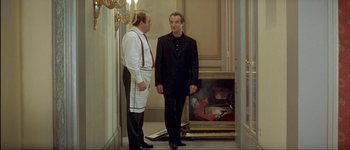 Movie still from “Le Dîner de Cons” (1998), directed by Francis Veber – Two men standing next to each other in front of a painting; Medium shot, Over the shoulder angle
