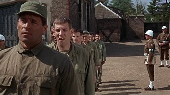 Movie still from “The Dirty Dozen” (1967), directed by Robert Aldrich – A group of men standing next to each other in front of a brick building; Medium shot, Over the shoulder angle