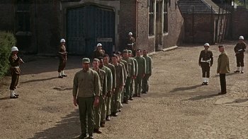 Movie still from “The Dirty Dozen” (1967), directed by Robert Aldrich – A group of men standing in front of a brick building; Wide shot, High angle