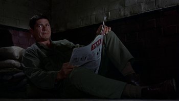 Movie still from “The Dirty Dozen” (1967), directed by Robert Aldrich – A man sitting on the ground reading a newspaper; Medium shot, Low angle