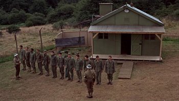 Movie still from “The Dirty Dozen” (1967), directed by Robert Aldrich – A group of men standing next to each other in front of a house; Extreme Wide shot, High angle