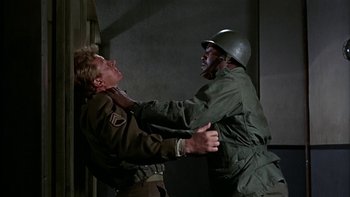 Movie still from “The Dirty Dozen” (1967), directed by Robert Aldrich – A man in a military uniform being held down by another man; Medium shot, Over the shoulder angle
