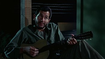 Movie still from “The Dirty Dozen” (1967), directed by Robert Aldrich – A man holding a guitar while sitting on a couch; Close Up shot, Low angle