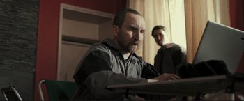 Movie still from “The Disappearance of Alice Creed” (2009), directed by J Blakeson – A man sitting at a table in front of a computer; Medium shot, Low angle