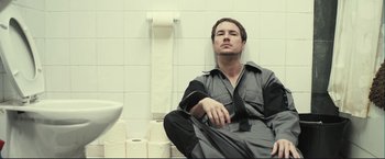 Movie still from “The Disappearance of Alice Creed” (2009), directed by J Blakeson – A man sitting on the floor of a bathroom next to toilet paper rolls; Medium shot, Low angle
