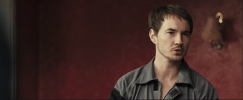 Movie still from “The Disappearance of Alice Creed” (2009), directed by J Blakeson – A young man is standing in front of a red background; Close Up shot, Low angle
