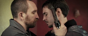 Movie still from “The Disappearance of Alice Creed” (2009), directed by J Blakeson – Two men one of whom is holding a gun and the other one is holding a gun in his hand; Close Up shot, Over the shoulder angle