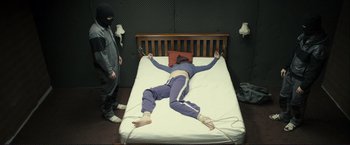 Movie still from “The Disappearance of Alice Creed” (2009), directed by J Blakeson – A person is tied up on a bed while another person watches; Wide shot, Overhead angle