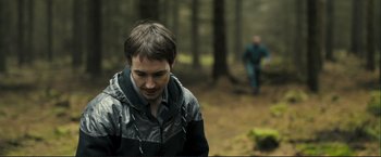 Movie still from “The Disappearance of Alice Creed” (2009), directed by J Blakeson – A young man in a jacket walking through the woods; Medium shot, Over the shoulder angle
