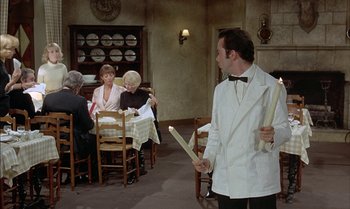 Movie still from “The Discreet Charm of the Bourgeoisie” (1972), directed by Luis Buñuel – A man in a white coat holding a stick in front of three women; Medium shot, Over the shoulder angle