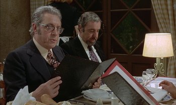 Movie still from “The Discreet Charm of the Bourgeoisie” (1972), directed by Luis Buñuel – A couple of men sitting down at a table; Medium shot, Over the shoulder angle