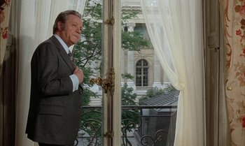 Movie still from “The Discreet Charm of the Bourgeoisie” (1972), directed by Luis Buñuel – An older man standing in front of a window; Medium shot, Low angle