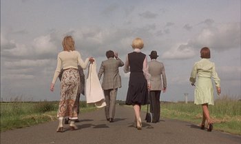 Movie still from “The Discreet Charm of the Bourgeoisie” (1972), directed by Luis Buñuel – A group of people walking down a road; Wide shot, Low angle