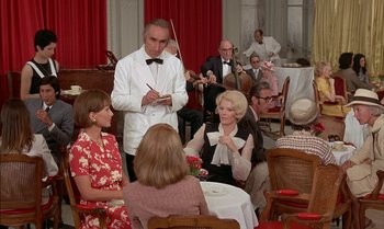 Movie still from “The Discreet Charm of the Bourgeoisie” (1972), directed by Luis Buñuel – A group of people sitting at a table in a restaurant; Wide shot, High angle