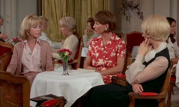 Movie still from “The Discreet Charm of the Bourgeoisie” (1972), directed by Luis Buñuel – A group of women sitting at a table with a vase filled with flowers; Medium shot, Over the shoulder angle