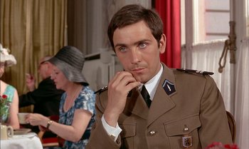 Movie still from “The Discreet Charm of the Bourgeoisie” (1972), directed by Luis Buñuel – A man in a military uniform is looking at the camera; Close Up shot, Over the shoulder angle