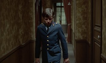 Movie still from “The Discreet Charm of the Bourgeoisie” (1972), directed by Luis Buñuel – A young boy in a uniform walking down a hallway; Medium shot, High angle