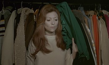 Movie still from “The Discreet Charm of the Bourgeoisie” (1972), directed by Luis Buñuel – A woman with long red hair holding a green jacket; Medium shot, High angle
