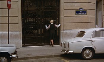 Movie still from “The Discreet Charm of the Bourgeoisie” (1972), directed by Luis Buñuel – An older woman in a black dress and white gloves; Wide shot, High angle