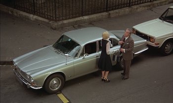 Movie still from “The Discreet Charm of the Bourgeoisie” (1972), directed by Luis Buñuel – A man and a woman standing in front of a silver car; Wide shot, High angle