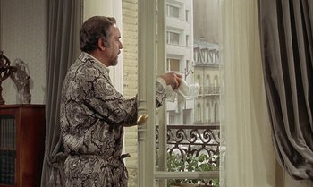 Movie still from “The Discreet Charm of the Bourgeoisie” (1972), directed by Luis Buñuel – A man wearing a robe is looking out of a window; Medium shot, Over the shoulder angle