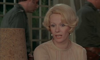 Movie still from “The Discreet Charm of the Bourgeoisie” (1972), directed by Luis Buñuel – An older woman with blonde hair sitting in front of a brick wall; Close Up shot, Over the shoulder angle