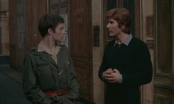 Movie still from “The Discreet Charm of the Bourgeoisie” (1972), directed by Luis Buñuel – Two men are standing next to each other talking; Medium shot, Over the shoulder angle