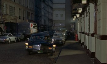 Movie still from “The Discreet Charm of the Bourgeoisie” (1972), directed by Luis Buñuel – A group of cars driving down a street at night; Extreme Wide shot, Over the shoulder angle