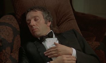 Movie still from “The Discreet Charm of the Bourgeoisie” (1972), directed by Luis Buñuel – A man in a tuxedo is sleeping on a couch; Medium shot, High angle