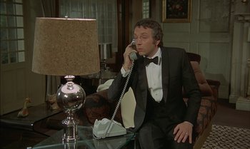 Movie still from “The Discreet Charm of the Bourgeoisie” (1972), directed by Luis Buñuel – A man sitting at a table talking on the phone; Medium shot, High angle