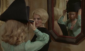 Movie still from “The Discreet Charm of the Bourgeoisie” (1972), directed by Luis Buñuel – A woman putting makeup on in front of a mirror; Close Up shot, Over the shoulder angle
