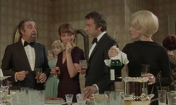Movie still from “The Discreet Charm of the Bourgeoisie” (1972), directed by Luis Buñuel – A group of people standing around a table with wine glasses; Medium shot, Over the shoulder angle