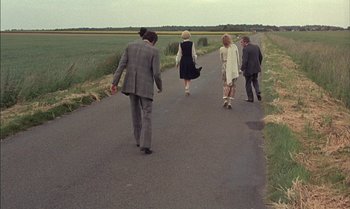 Movie still from “The Discreet Charm of the Bourgeoisie” (1972), directed by Luis Buñuel – A group of people walking down a road; Wide shot, High angle