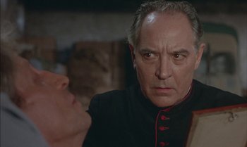 Movie still from “The Discreet Charm of the Bourgeoisie” (1972), directed by Luis Buñuel – An older man in a black and red uniform looking at another older man; Close Up shot, Over the shoulder angle