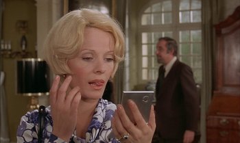 Movie still from “The Discreet Charm of the Bourgeoisie” (1972), directed by Luis Buñuel – A woman looking at a cell phone while standing in front of a man; Close Up shot, Low angle