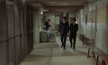 Movie still from “The Discreet Charm of the Bourgeoisie” (1972), directed by Luis Buñuel – A couple of men walking down a hall way; Wide shot, High angle