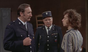 Movie still from “The Discreet Charm of the Bourgeoisie” (1972), directed by Luis Buñuel – A group of men standing next to each other in uniform; Medium shot, Over the shoulder angle