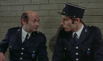 Movie still from “The Discreet Charm of the Bourgeoisie” (1972), directed by Luis Buñuel – Two men in uniform talking to each other; Medium shot, High angle