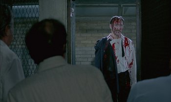 Movie still from “The Discreet Charm of the Bourgeoisie” (1972), directed by Luis Buñuel – A man with blood all over his face is standing in front of another man; Medium shot, Over the shoulder angle