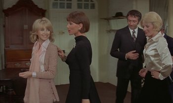 Movie still from “The Discreet Charm of the Bourgeoisie” (1972), directed by Luis Buñuel – Two women and a man standing in a room; Medium shot, Over the shoulder angle