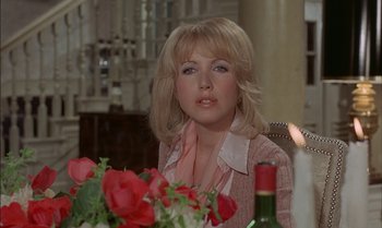 Movie still from “The Discreet Charm of the Bourgeoisie” (1972), directed by Luis Buñuel – A woman sitting in front of a table with a vase of flowers; Close Up shot, Over the shoulder angle