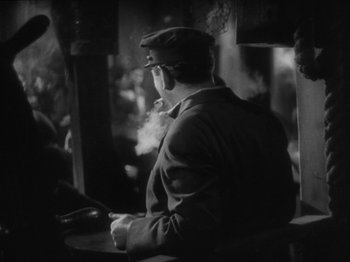 Movie still from “The Docks of New York” (1928), directed by Josef von Sternberg – A black and white photo of a man smoking a pipe; Medium shot, Over the shoulder angle