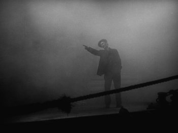 Movie still from “The Docks of New York” (1928), directed by Josef von Sternberg – A man in a suit and hat pointing in the fog; Wide shot, Low angle