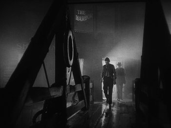 Movie still from “The Docks of New York” (1928), directed by Josef von Sternberg – A man walking in a dark room with a camera in his hand; Wide shot, Low angle
