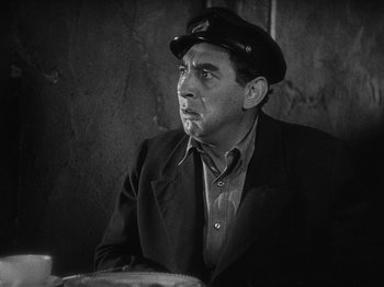 Movie still from “The Docks of New York” (1928), directed by Josef von Sternberg – An older man wearing a hat sitting at a table in front of a wall; Close Up shot, High angle